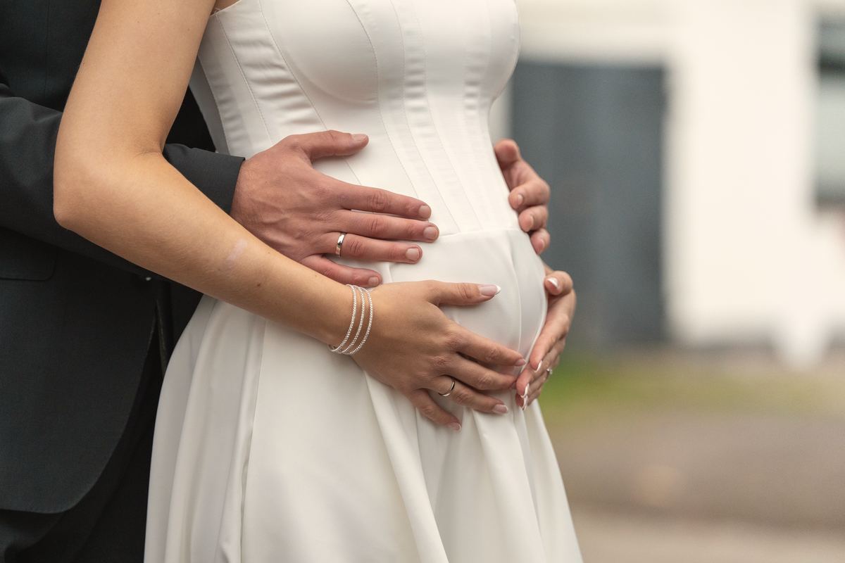 Hände mit Eheringen auf dem Bauch der schwangeren Braut.